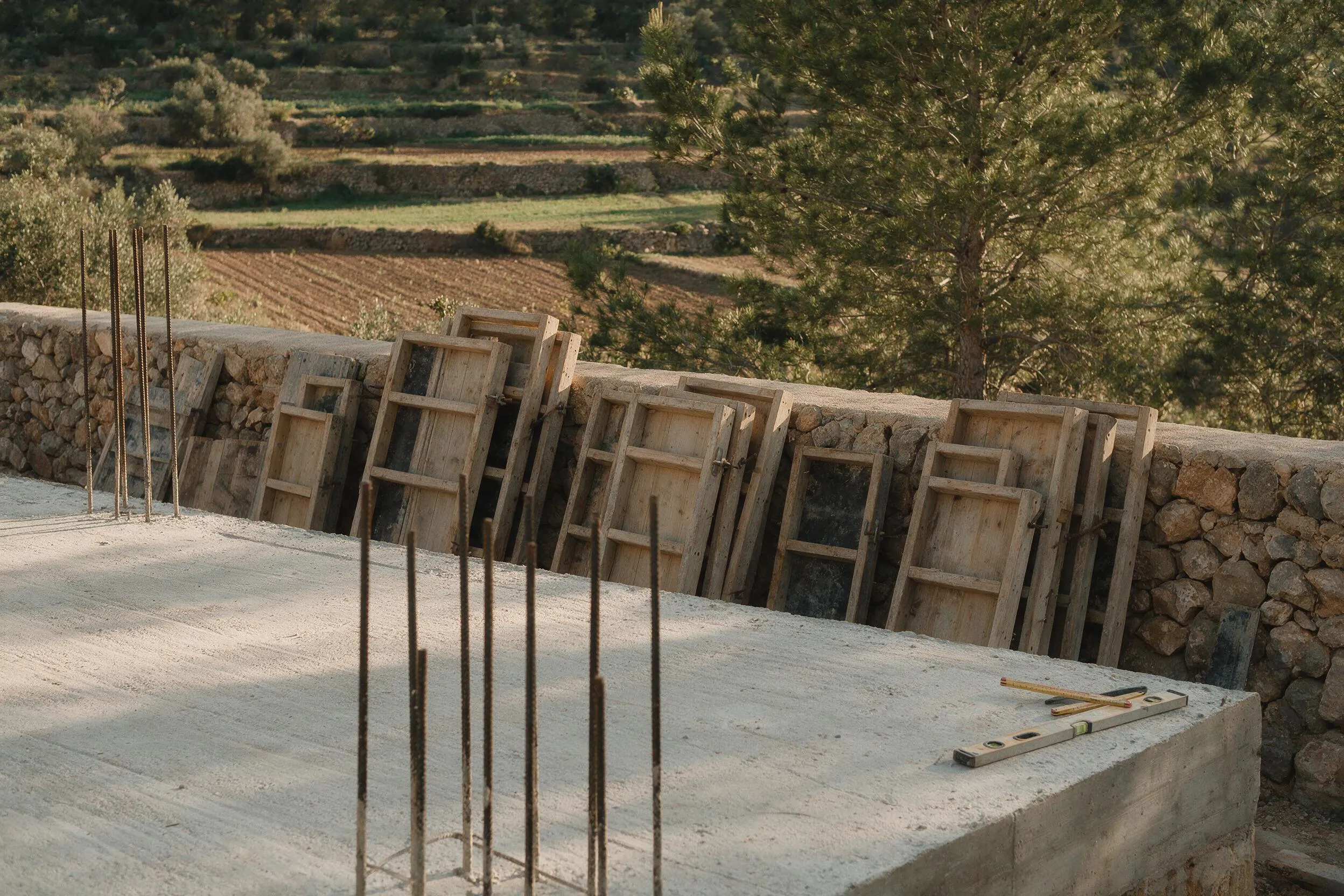Forjado de hormigón recién ejecutado con esperas de acero y paneles de encofrado apoyados en un muro de piedra seca