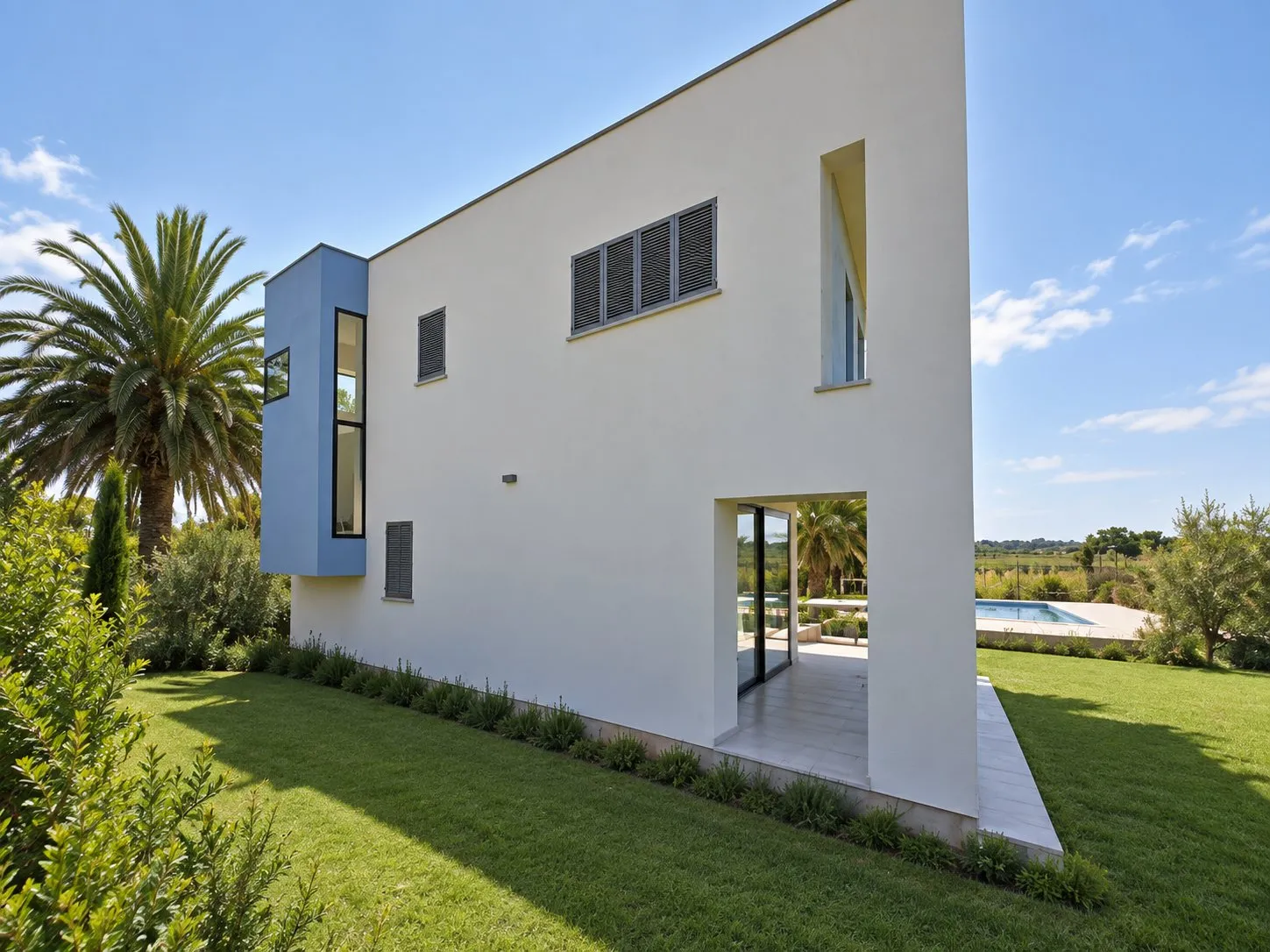 Fachada lateral blanca de la vivienda Salbufereta, con el jardín y la piscina al fondo