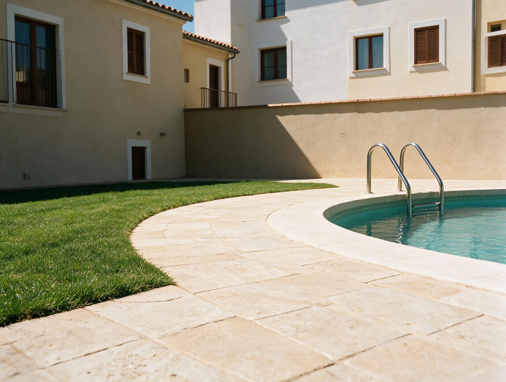 Encuentro entre el pavimento de piedra del patio, el césped y el borde de la piscina